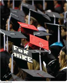 A photo shows a close-up shot of numerous students in graduation hats. A text on one of the graduation hats reads, For Hire.