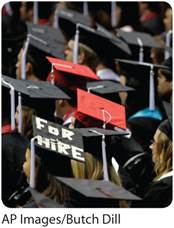 A photo shows a close-up shot of numerous students in graduation hats. A text on one of the graduation hats reads, For Hire.