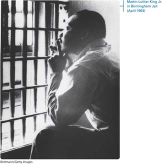 A black and white photo shows Martin Luther King Junior sitting behind the bars of Birmingham jail and looking at the distance. A margin note reads, Martin Luther King Junior in Birmingham Jail. April 1963.