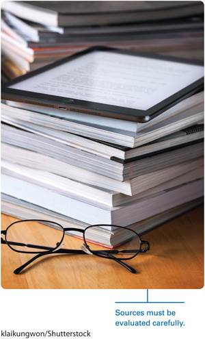A photo shows a tablet lying on a pile of books, and a pair of glasses in front of it.