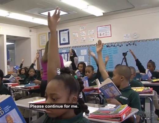 Photo depicts students raising their hands in a classroom.