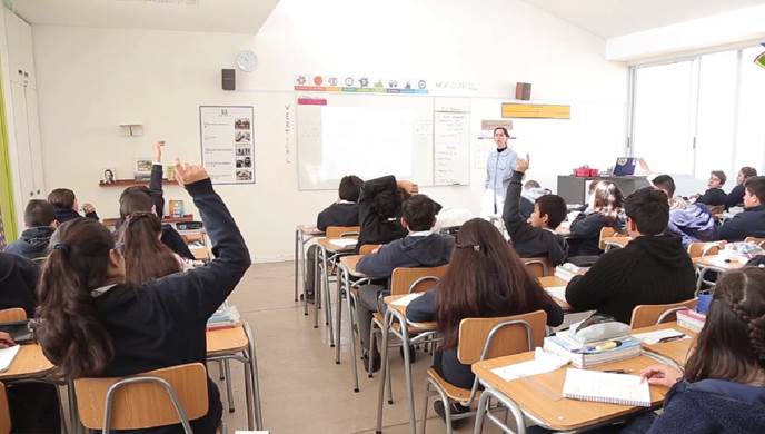Photo depicts a few of the students raising their hands in a class room.
