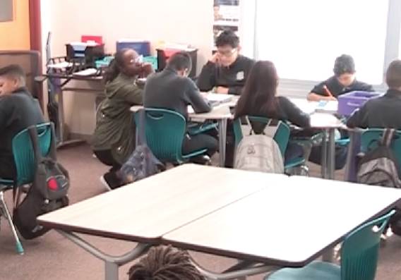 Photo depicts students sitting around a table and looking at their books.